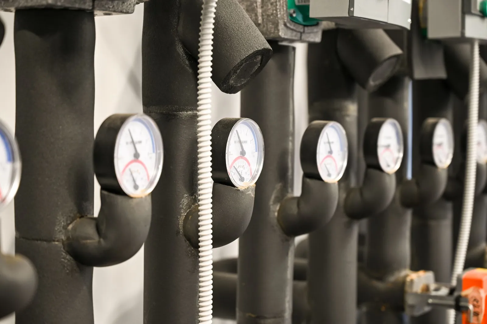 Pressure gauges on insulated hot water heating pipes in a boiler room