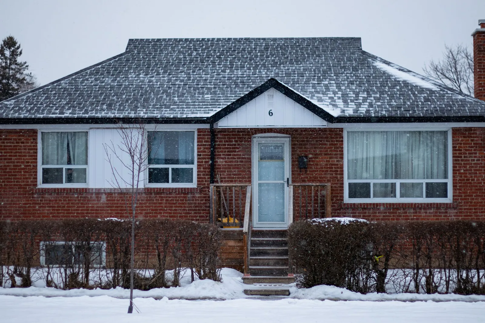 Brick ranch house with a snow-covered roof and deep snow in the front yard